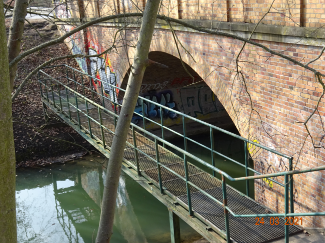 Fußgängerbrücke neben der Hoppendorfer Straßenbrücke / Wuhle, vor der Bogenbrücke hinter den Sträuchern
