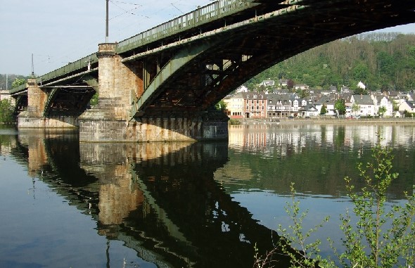 Das Foto zeigt die Stahlbögen unterhalb der Trassenkonstruktion, die beiden in der Mosel stehenden Pfeiler sowie einige unmittelbar an der B416 gelegene Häuser des Koblenzer Stadtteils Güls.